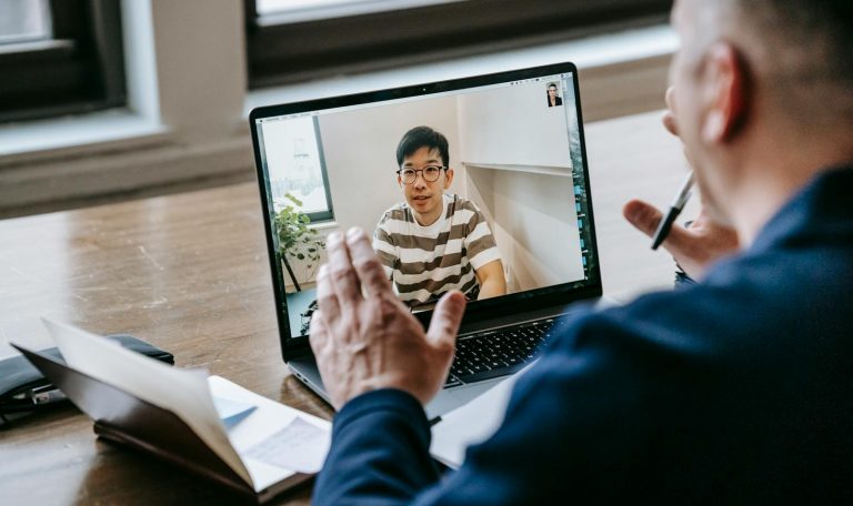 Two professionals engaged in an online video conference on a laptop in an indoor setting.
