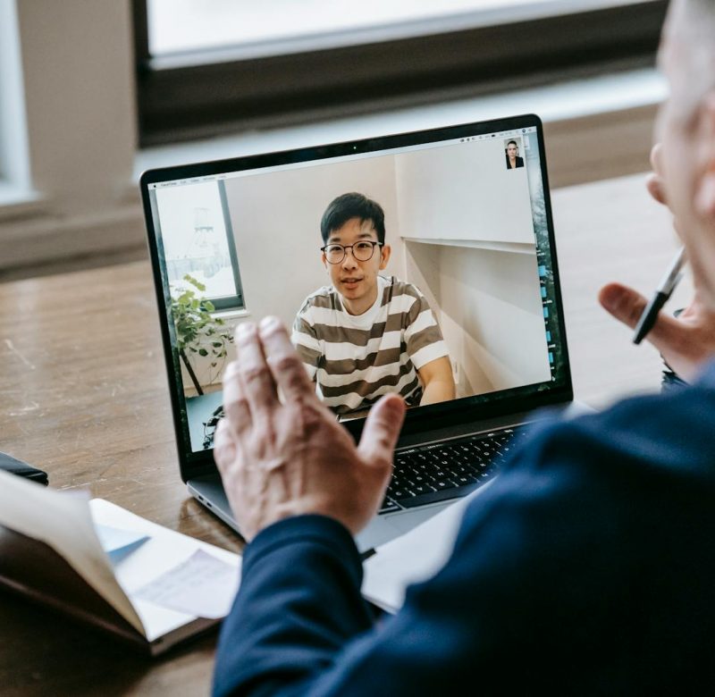 Two professionals engaged in an online video conference on a laptop in an indoor setting.